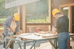 Carpenters working with power tools outdoors under sunlight.